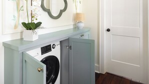 Una sala de lavandería con lavadora, un espejo y una mesita con lámpara.