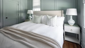 Un dormitorio ordenado con una cama grande, dos mesitas de noche con lámparas y una ventana con persiana blanca.