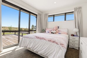 A bedroom with a large bed, a nightstand, and a view of the outdoors. - Tranquil and Unique In A Gated Grandview Estate Community With Amazing Views (Taupō)