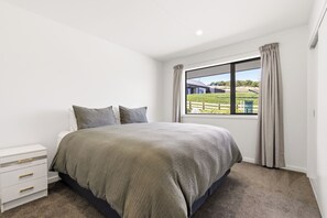 A bedroom with a large bed, a nightstand, a window with curtains, and a view of a building outside. - Tranquil and Unique In A Gated Grandview Estate Community With Amazing Views (Taupō)