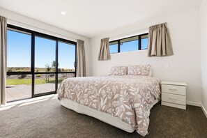 A bedroom with a large sliding glass door leading to a patio, a bed with floral bedding, and a nightstand with drawers.