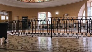 Een statige hal met een groot glas-in-lood plafond, een betegelde vloer en een smeedijzeren balustrade.