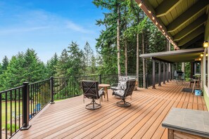 A wooden deck with two chairs and a small table, surrounded by a railing and overlooking a forest.