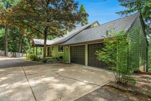 A green house with a garage, driveway, and surrounding trees.