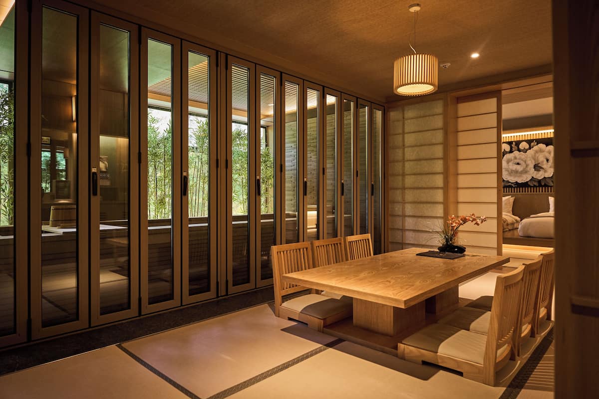 A modern dining area with a wooden table and chairs, a vase with flowers, and a view through large glass doors.
