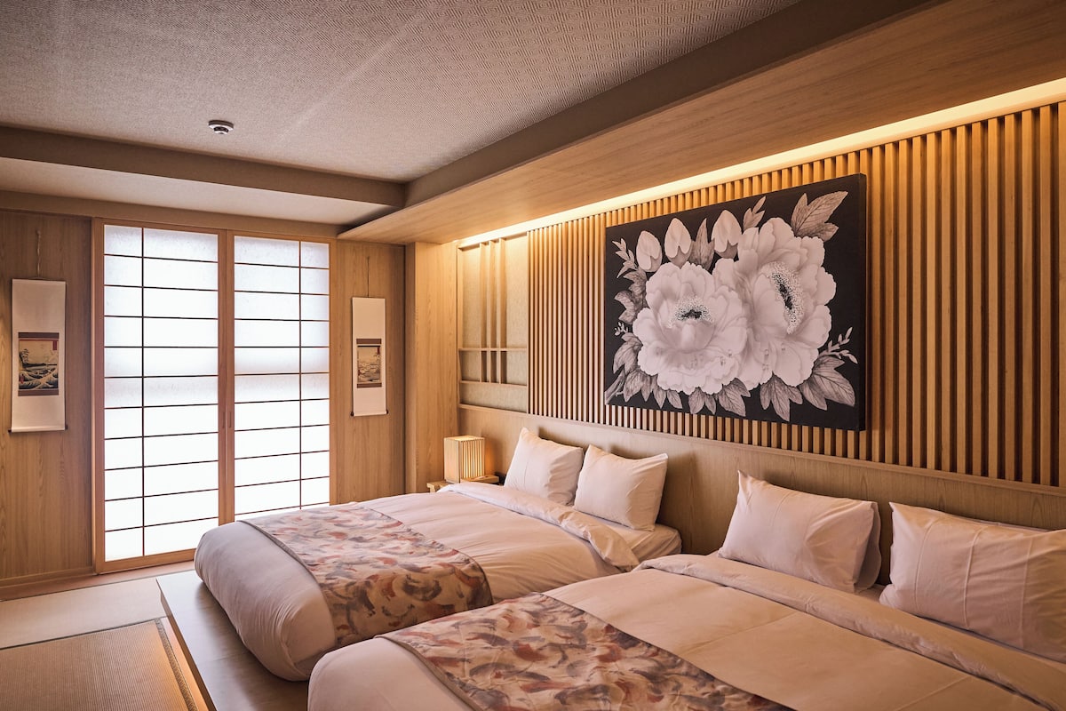A traditional Japanese-style bedroom with tatami flooring, two beds with floral bedding, a large floral artwork on the wall, and sliding doors.