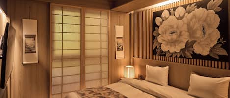 Ein traditionell gestaltetes japanisches Schlafzimmer mit Schiebetüren, einer großen Blumenmalerei und einem Bett mit gemusterten Betttextilien.