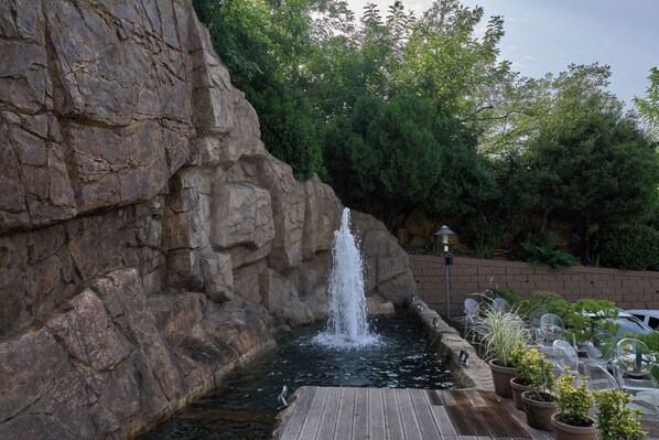 Une cascade artificielle en roche, agrémentée d’une terrasse en bois et de plantes en pot.