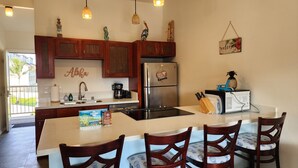Una cocina con armarios de madera, un refrigerador de acero inoxidable, una cafetera y un comedor con sillas de madera.