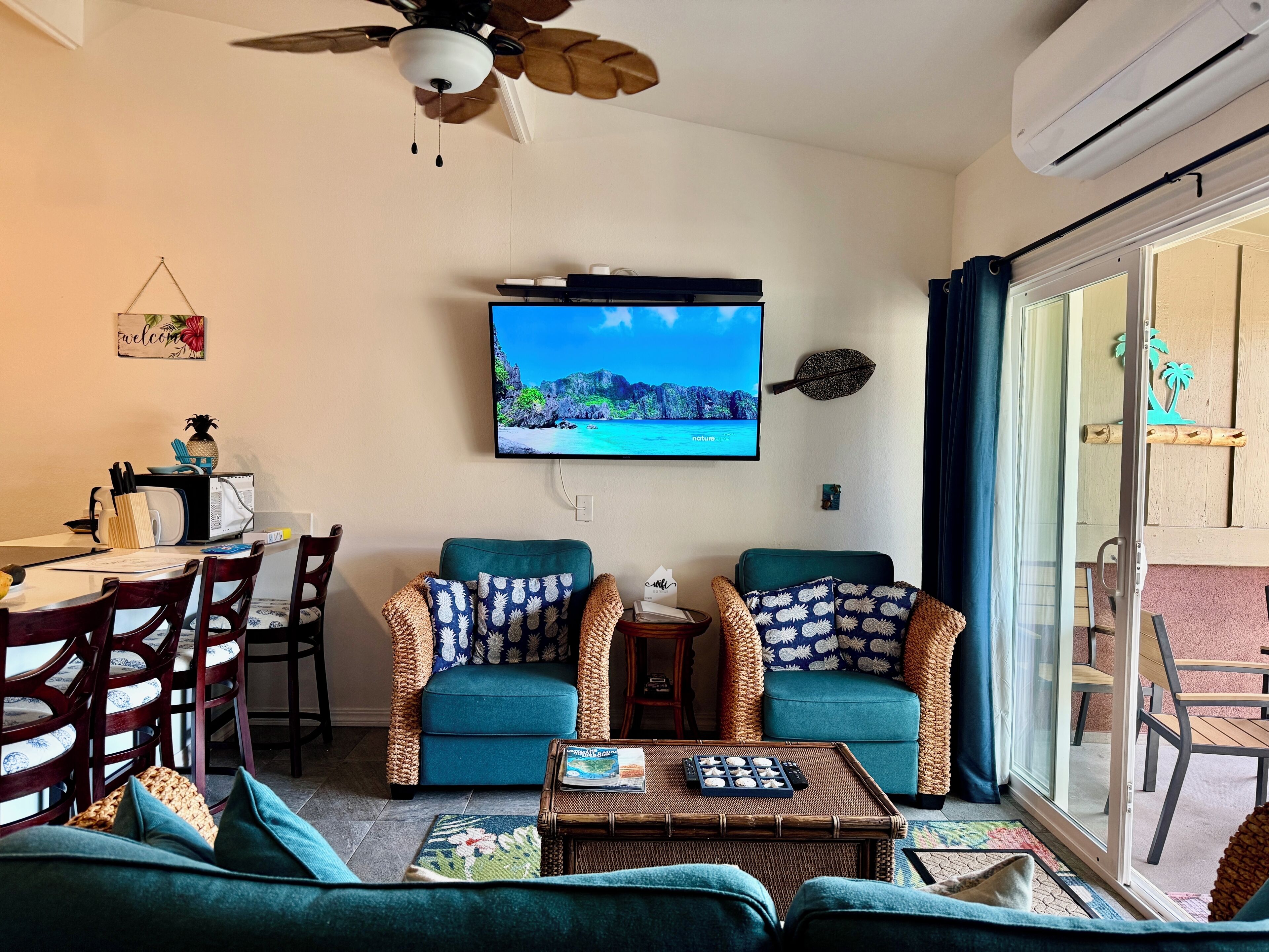 A living room with two teal sofas, a coffee table, a TV, and a ceiling fan.