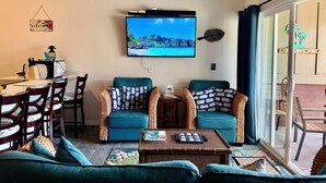 Una sala de estar con dos sofás color turquesa, una mesa de centro, un televisor y un ventilador de techo.