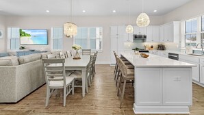 A modern kitchen with white cabinetry, a large island, and pendant lighting. - 209 Seabreeze Escape: NEW 5BR Pool Home, Close to Beach! (Fort Myers Beach)