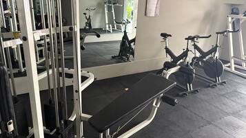 A gym with various exercise equipment, a mirror, and a television on the wall.