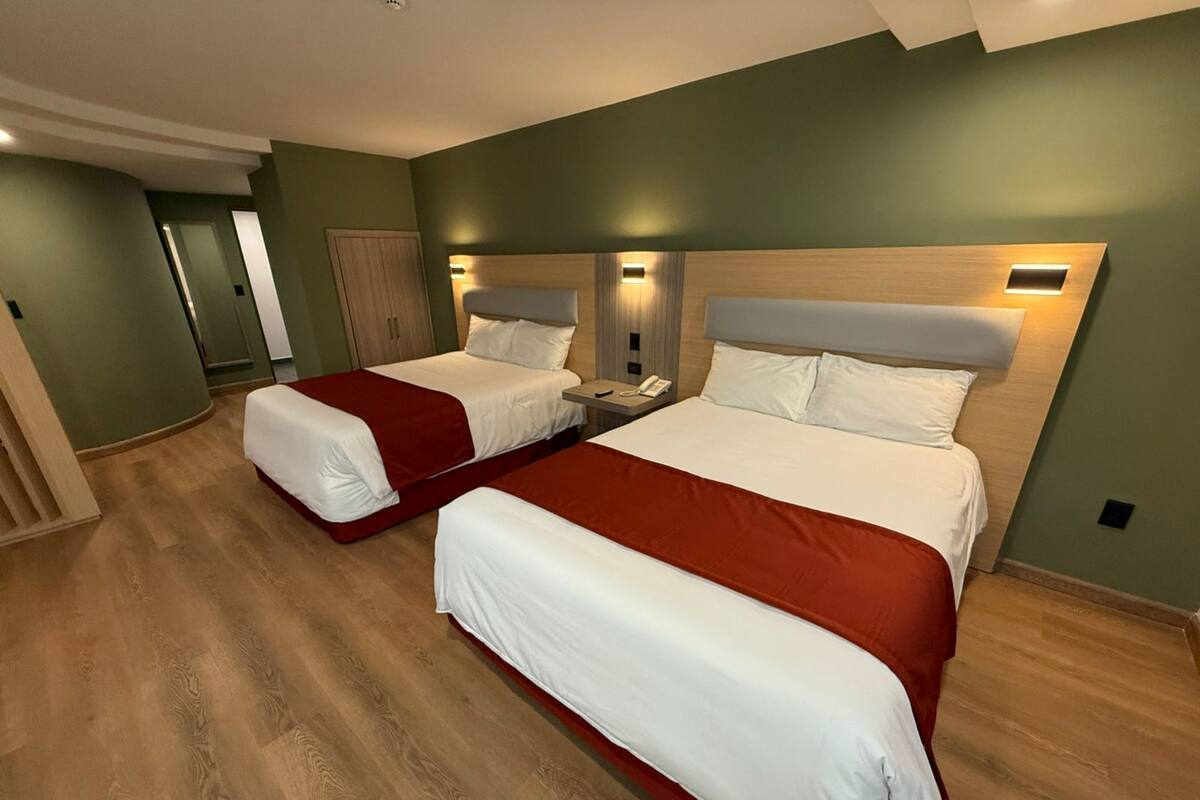 Une chambre d’hôtel avec deux lits, chacun recouvert d’une courtepointe rouge et blanche, dotés de têtes de lit en bois et de lampes de chevet.