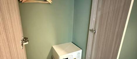 A compact room with a wooden wardrobe, a small white cabinet, and a wooden hanger.
