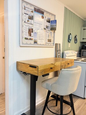 Una cocina con una mesa de madera, una silla y un tablón de anuncios con varios avisos.