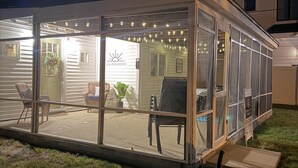 Un'area esterna vetrata con patio, posti a sedere e luci decorative.
