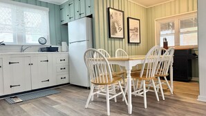 Cucina con mobili bianchi, frigorifero, tavolo da pranzo con sedie e quadri appesi al muro.