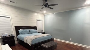 A bedroom with a bed, nightstands, a ceiling fan, and a washing machine.