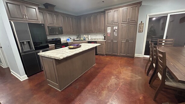 A kitchen with a large island, dark wood cabinets, a refrigerator, and a dining area with chairs.