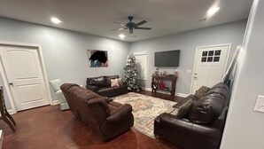 A living room with two leather sofas, a coffee table, a Christmas tree, and a flat-screen TV mounted on the wall.