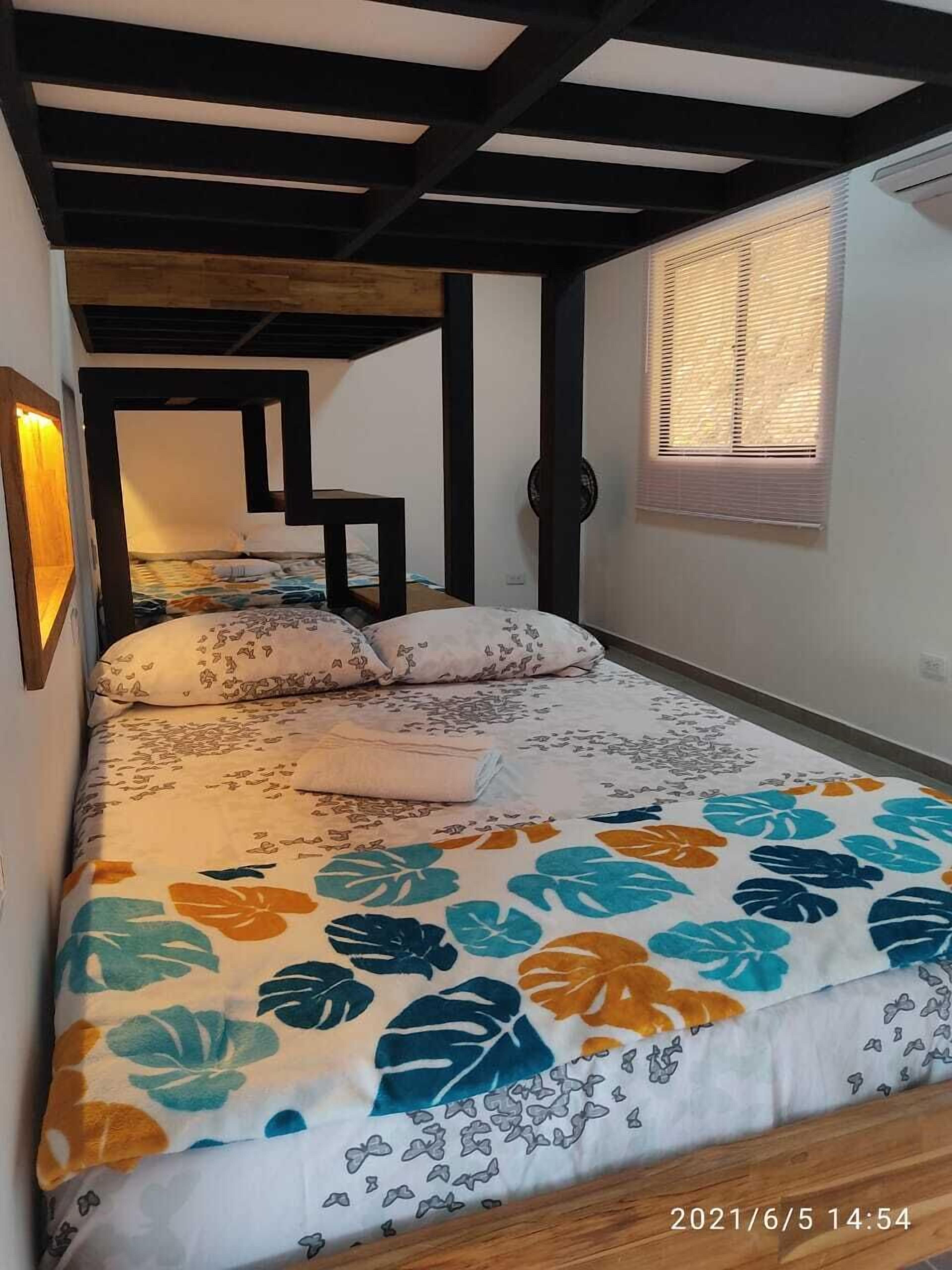 Un dormitorio con una cama, un ventanal con persianas y una estructura de techo de madera.
