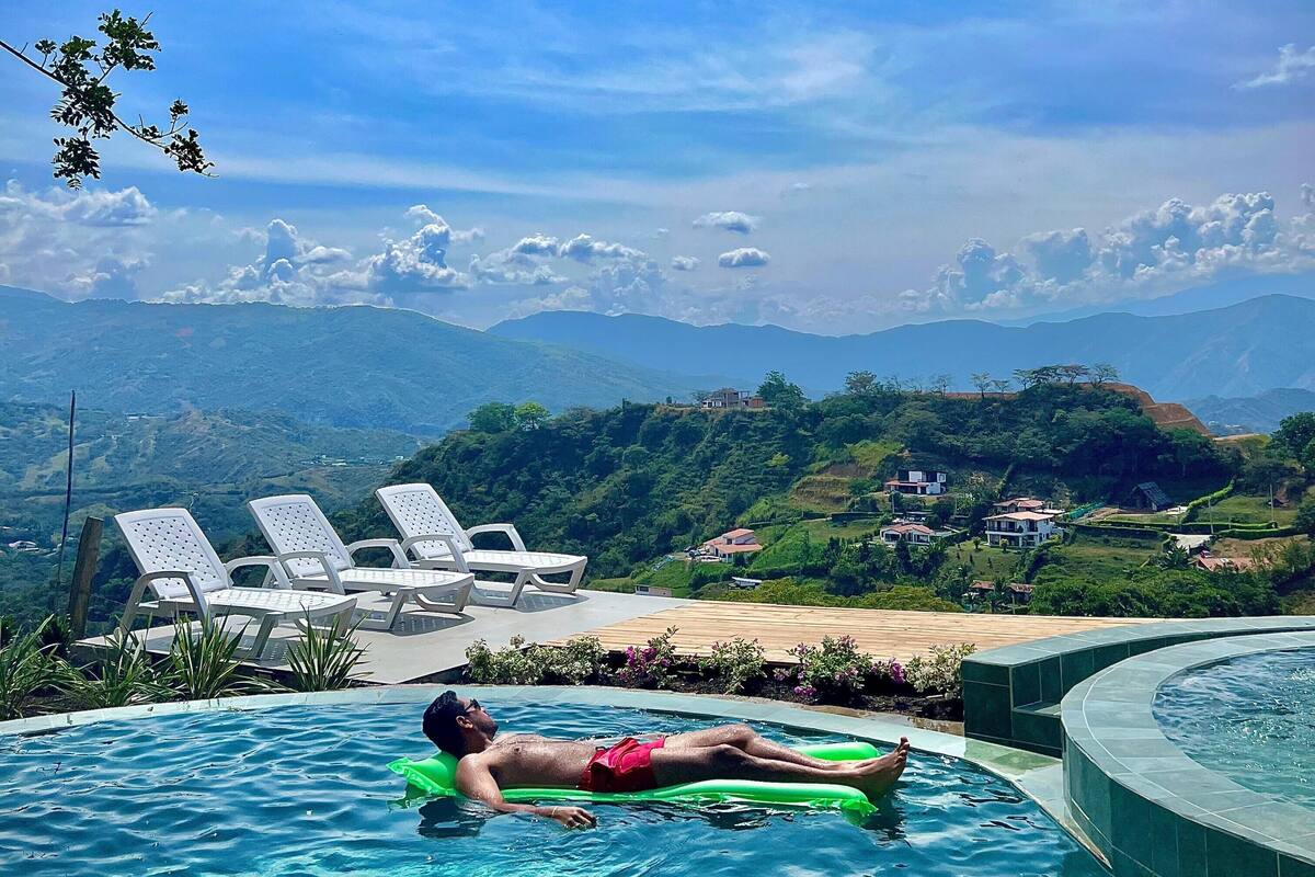 Ein Mann entspannt auf einer Schwimminsel in einem Pool mit Blick auf eine malerische Berglandschaft.