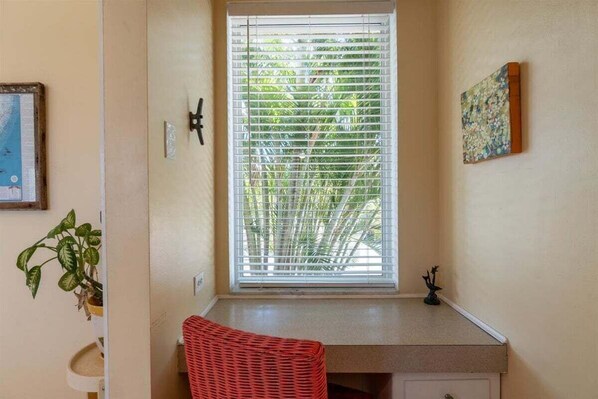 A room with a window, a red chair, a small table, and a painting on the wall.