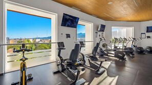 A gym with various exercise machines, large windows with a city view, and a wooden ceiling.