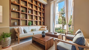 A living room with a wooden bookshelf, a sofa, a coffee table, and a view of the outdoors through large windows. - Gorgeous 1BR with Pools & Sea Views (Puerto Vallarta)