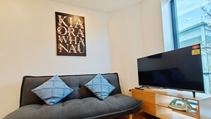 A modern living room with a grey sofa, two decorative pillows, a flat-screen TV, and a wooden side table with an iron.