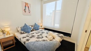 A bedroom with a bed, two nightstands, a window, and a wall-mounted picture.
