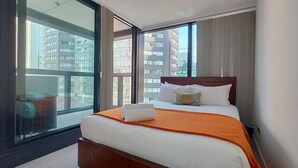 Habitación de hotel con una cama grande, vista a edificios altos y puerta corrediza al balcón.