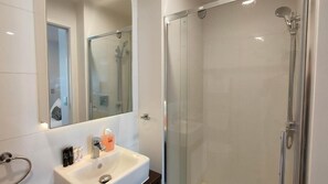 Une salle de bain moderne avec une douche à parois de verre, un lavabo blanc agrémenté d’articles de toilette et un grand miroir.