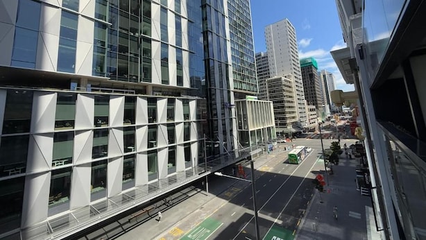 Una calle urbana moderna con edificios altos, una senda peatonal y un carril bus verde.