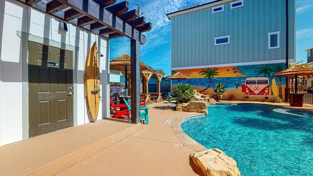 A pool area with a wooden door, a surfboard, and a mural of a beach scene. - Pet Friendly, Shared Heated Pool, Golf Cart Included (Port Aransas)