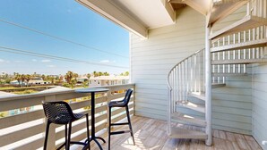 A balcony with a spiral staircase, two chairs, and a small table. - Pet Friendly, Shared Heated Pool, Golf Cart Included (Port Aransas)