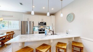 A kitchen with white cabinets, stainless steel appliances, and a marble island with bar stools. - Pet Friendly, Shared Heated Pool, Golf Cart Included (Port Aransas)
