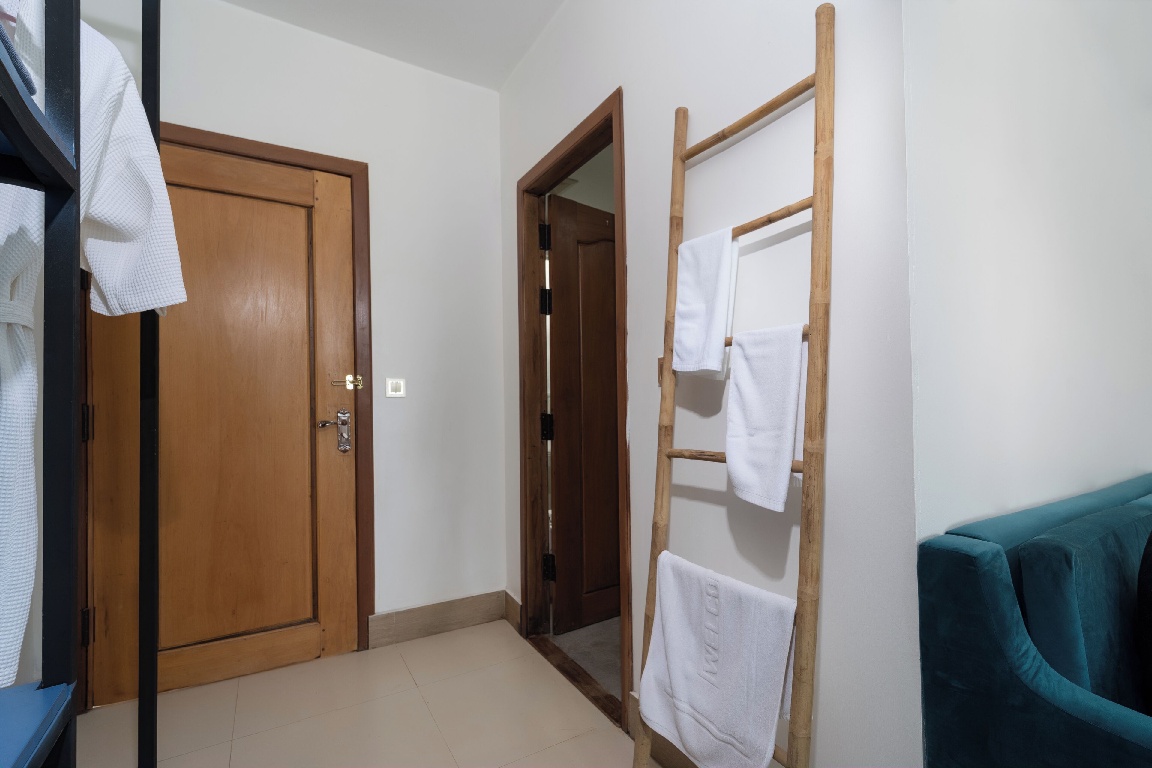 A hallway with a wooden door, a wooden towel rack, and a teal sofa.