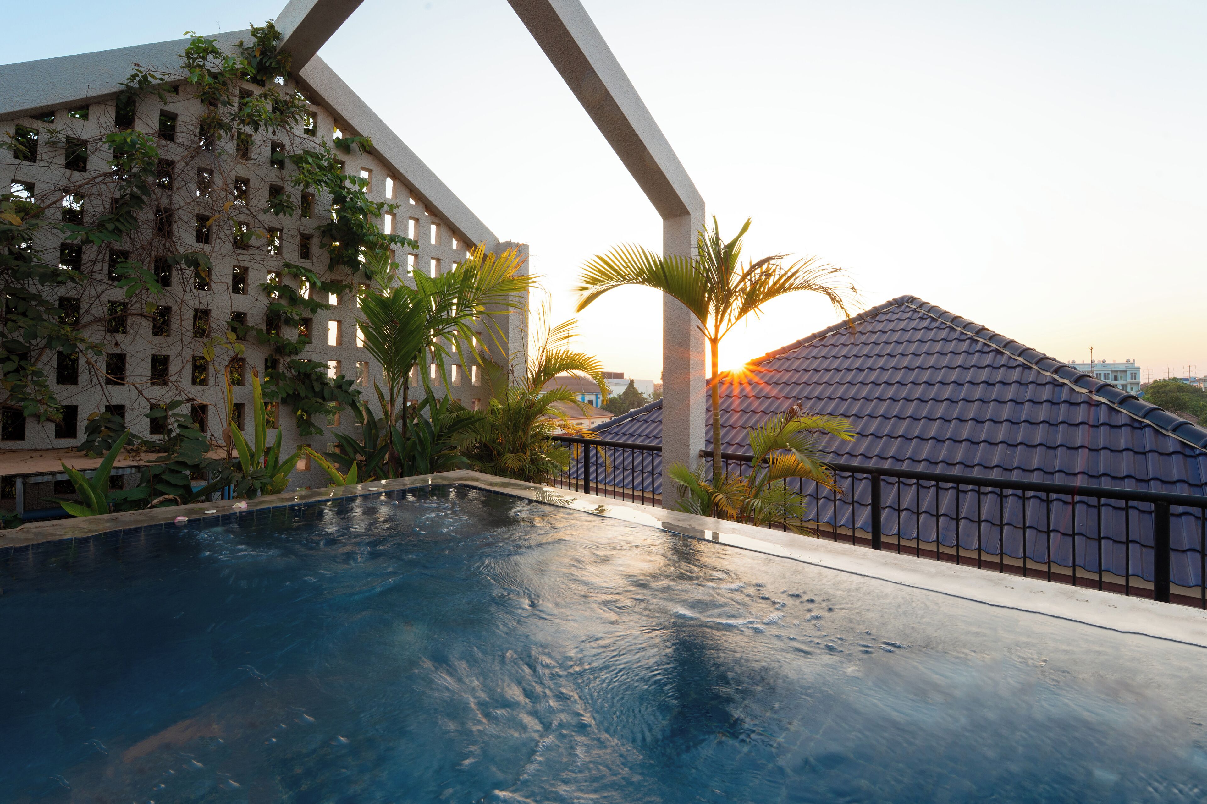 Une piscine à débordement offrant une vue sur un bâtiment doté d’un toit recouvert de tuiles et sur un palmier.