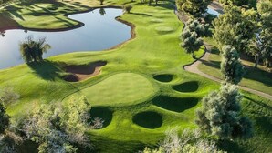 A golf course with a pond, trees, and a clear sky.