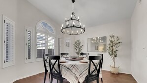 A dining area with a chandelier, wooden chairs, a table with a plaid tablecloth, and a potted plant.