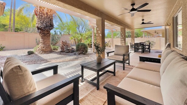 A covered patio area with outdoor furniture, a ceiling fan, and a view of a landscaped garden.