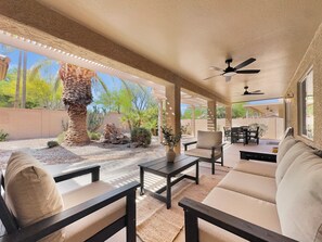 A covered patio area with outdoor furniture, a ceiling fan, and a view of a landscaped garden.