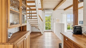 A wooden interior with a staircase, a kitchen area, and a view through a door. - Luxury holiday home with sea view (Svaneke)