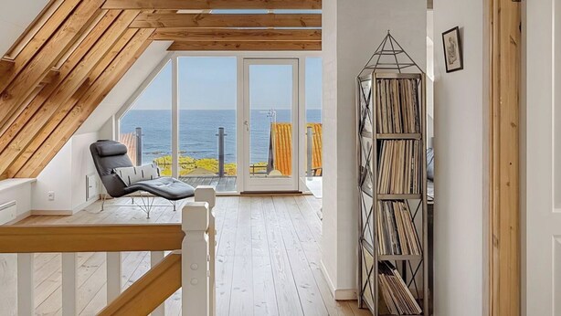 A room with a sloped ceiling, a view of the sea, a bookshelf, and a chair. - Luxury holiday home with sea view (Svaneke)