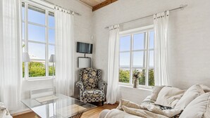 A room with a glass table, a patterned armchair, a sofa, and a TV on the wall. - Luxury holiday home with sea view (Svaneke)