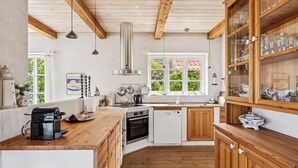 A kitchen with wooden beams, a built-in oven, a dishwasher, and a wooden cabinet with glass doors. - Luxury holiday home with sea view (Svaneke)