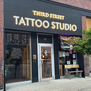 A storefront with a sign reading 'Third Street Tattoo Studio' and a window displaying a tattoo. - Luxury 2-bedroom apartment in downtown Elkins. (Elkins)