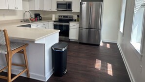 Una cocina moderna con armarios blancos, electrodomésticos de acero inoxidable, una silla de madera y un cubo de basura.